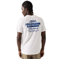 A man wearing a white Levi's short-sleeve t-shirt, viewed from the back. The shirt features a prominent blue graphic print of the 'Levi Strauss & Company' logo and original address on the back.