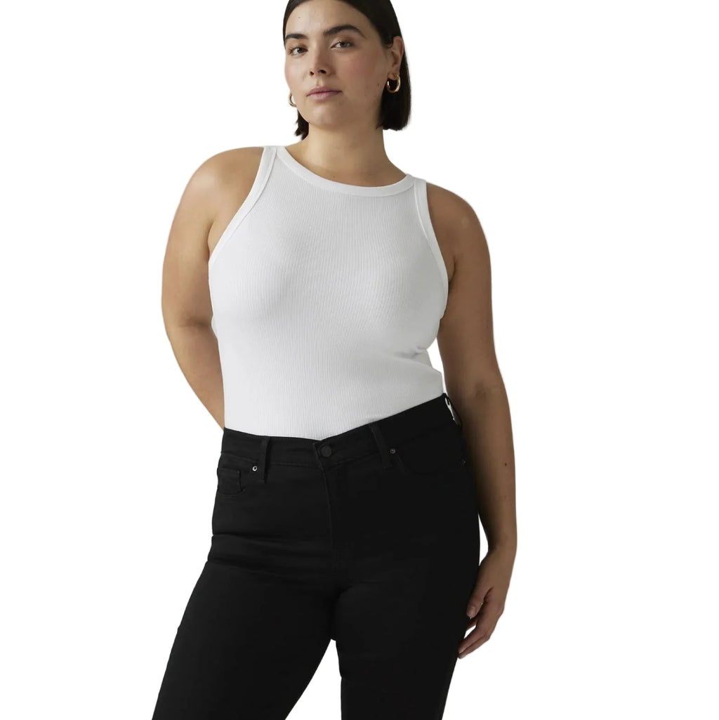 A woman modeling a fitted white ribbed tank top paired with black jeans, photographed against a plain white studio background.