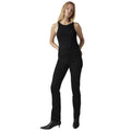 A woman modeling black sleeveless top and black slim-fit jeans with black pointed-toe ankle boots, standing against a white studio background.