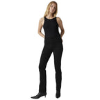 A woman modeling black sleeveless top and black slim-fit jeans with black pointed-toe ankle boots, standing against a white studio background.