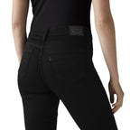 Rear view of a model wearing black skinny jeans with a black ribbed top, showing the back pockets and waistband patch of the jeans against a white background.
