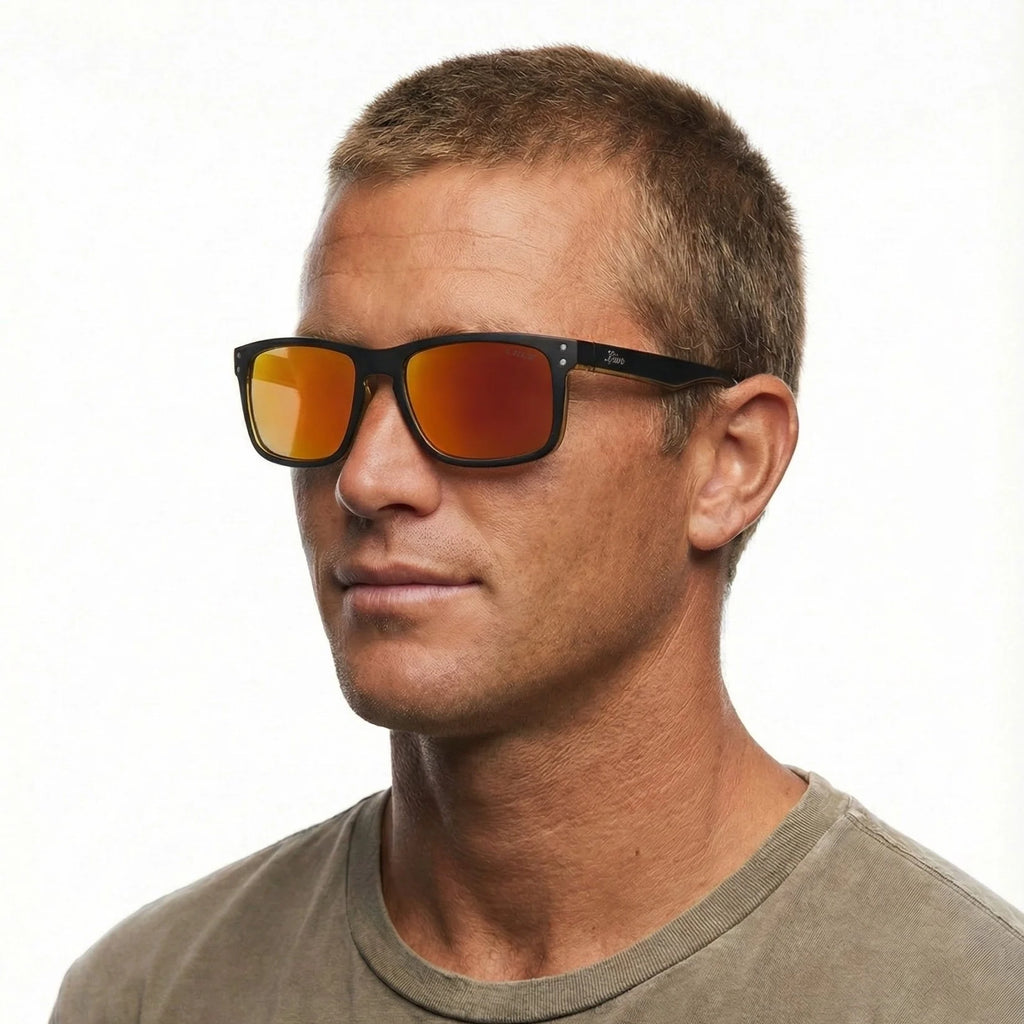 A head shot of a man modelling a pair  of Liive Vision Cheap Thrill Sunglasses (L0356A) with mirror orange lenses and black frames with orange accents on a white background.
