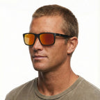 A head shot of a man modelling a pair  of Liive Vision Cheap Thrill Sunglasses (L0356A) with mirror orange lenses and black frames with orange accents on a white background.