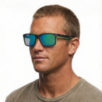 A man modelling Liive Vision Cheap Thrill Sunglasses (L0356K) in matte black with vibrant lime green accents along the temples and lower rims, and mirrored green lenses on a white background.