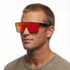 A headshot of a man modelling a pair of Liive Vision Wasteland Sunglasses (L0828A) with red mirror lenses and black and red frames, on a white background.