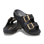 The Crocs Womens Saturday Metallic Buckle Sandals (213316-001) in black feature two wide straps per shoe with large gold metallic buckles, textured footbeds, and slightly elevated heels for added comfort and style.