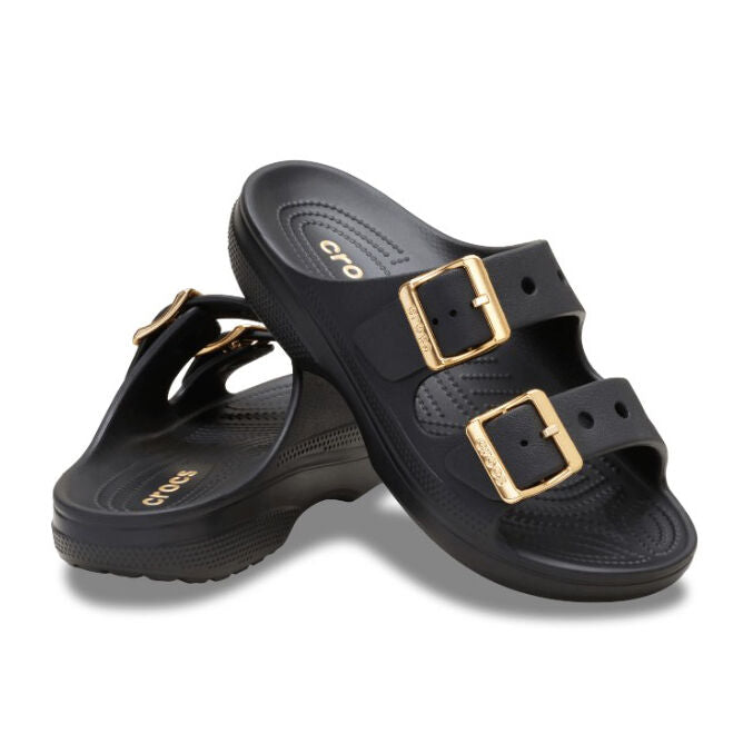 The Crocs Womens Saturday Metallic Buckle Sandals (213316-001) in black feature two wide straps per shoe with large gold metallic buckles, textured footbeds, and slightly elevated heels for added comfort and style.