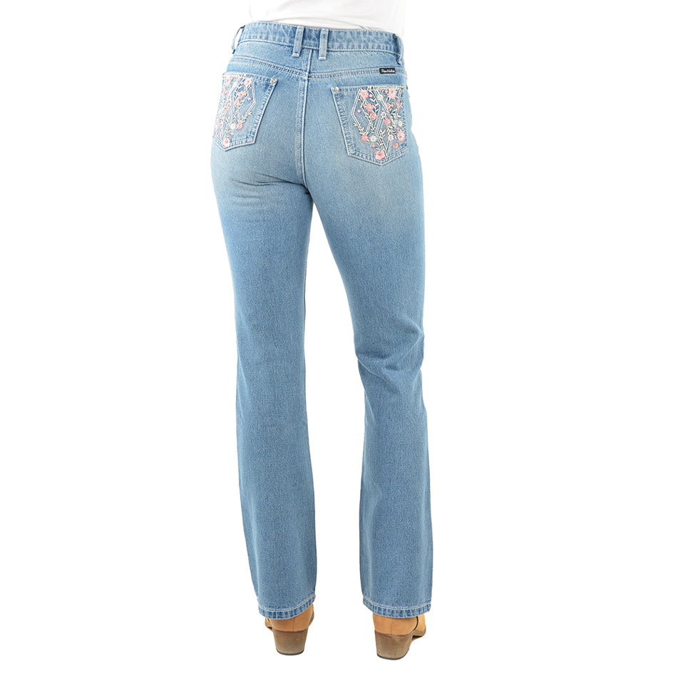 Rear view of a pair of light blue denim Pure Western High Rise Flora Bootcut Jeans (PCP2213725) with floral embroidery on the back pockets, worn by a model with brown heels against a white background.