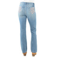Rear view of a pair of light blue denim Pure Western High Rise Flora Bootcut Jeans (PCP2213725) with floral embroidery on the back pockets, worn by a model with brown heels against a white background.