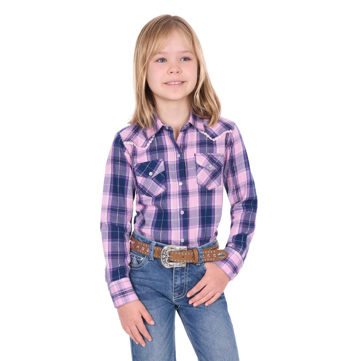 A young girl with blonde hair wears the Pure Western Girls Arleen L/S Shirt (P6W5527199) in Pink/Navy, along with jeans and a brown belt, standing and smiling against a white background.