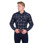 A man wearing the Pure Western Mens Harley L/S Shirt (P6W1100166) in Navy/Tan and dark jeans stands against a white background, looking to the side with his hands on his belt buckle.