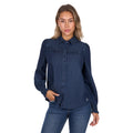 A woman confidently poses against a white background wearing the Pure Western Womens Daniela L/S Shirt (P6W2598204) in blue, paired with blue jeans, one hand touching her shirt.