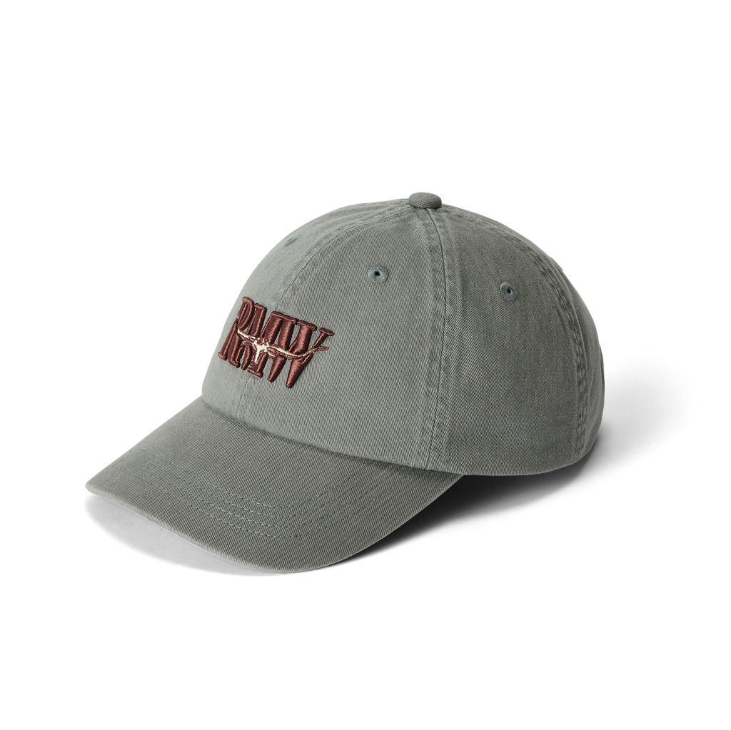 The R.M.Williams Heritage Twill Cap (ACX9OWI27) in slate is made from organic cotton twill and features embroidered red and white "DAILY REVV" text on the front, shown against a white background.