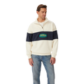 A man stands against a white background wearing the R.M.Williams Men's 90s Logo 1/4 Zip Jumper in ecru with a navy chest and sleeve stripe, paired with light blue jeans.
