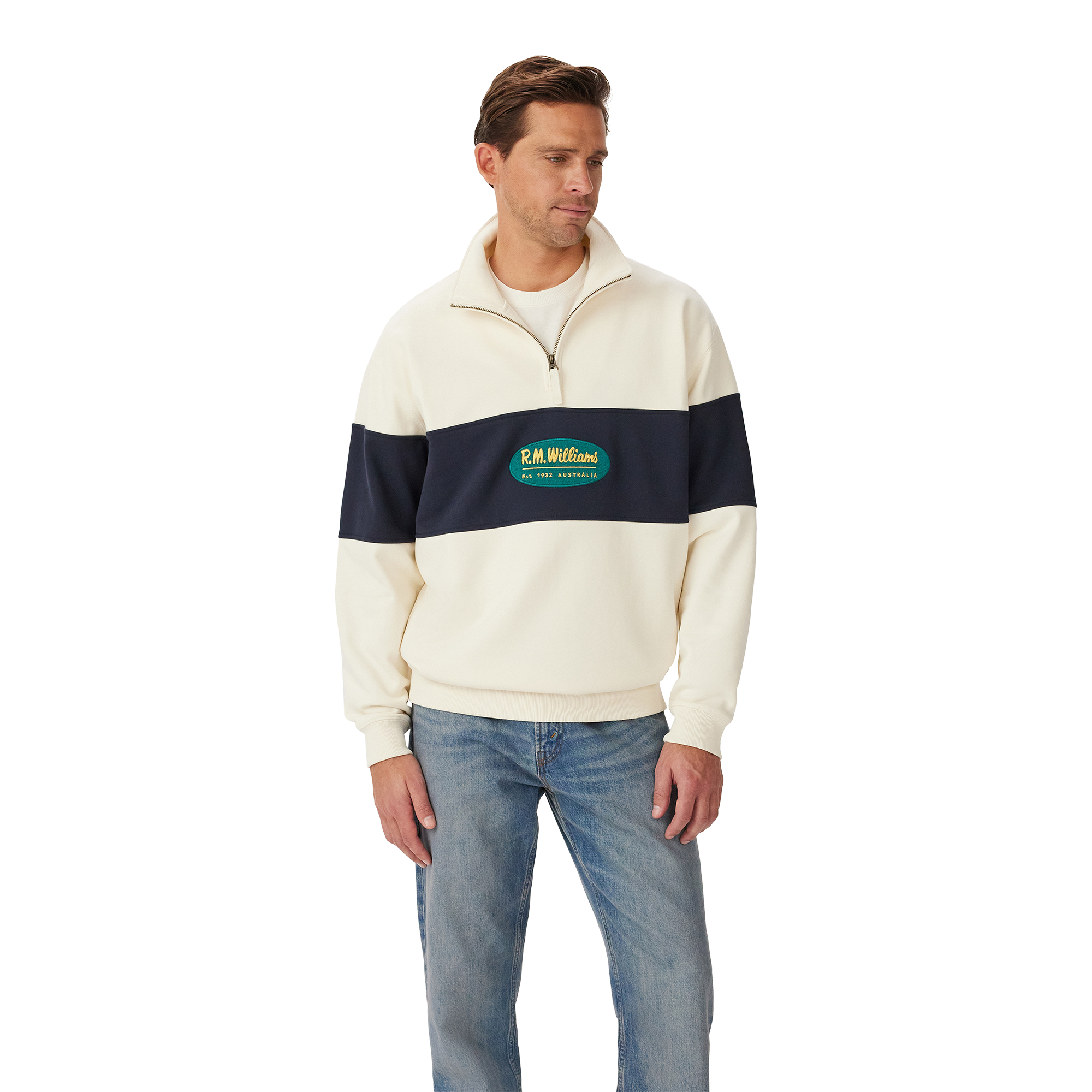 A man stands against a white background wearing the R.M.Williams Men's 90s Logo 1/4 Zip Jumper in ecru with a navy chest and sleeve stripe, paired with light blue jeans.
