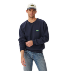 A man stands against a plain white background wearing a vintage navy R.M.Williams Mens 90s Logo Crew Jumper (KCU00BB01), light blue jeans, and a light gray cap.