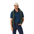 A man in a beige cap, dark jeans, and green sweater draped over his shoulders stands against a white background wearing the R.M.Williams Mens Albany Stripe Polo (KP210QS10) in Vintage Blue for a classic, relaxed look.