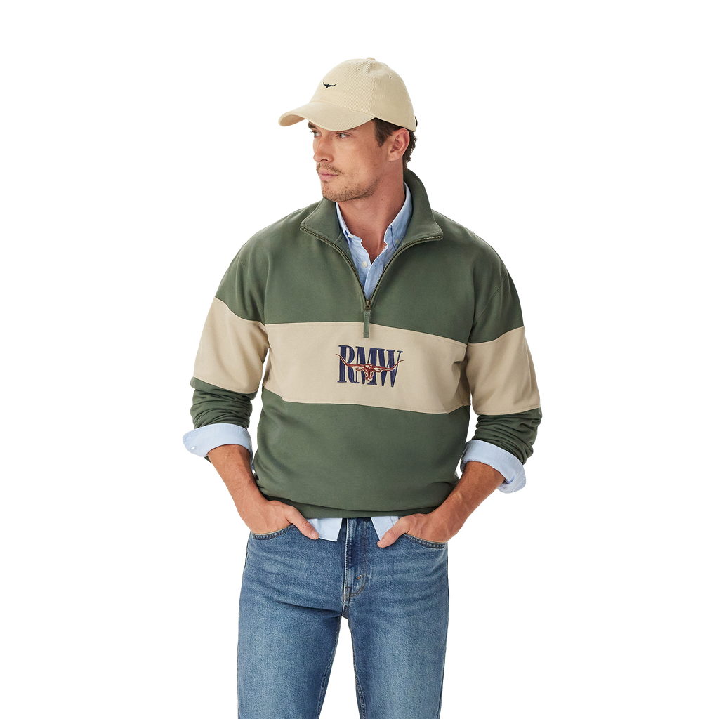 A man in a beige cap, blue jeans, and a light blue shirt layered under the R.M.Williams Mens Heritage 1/4 Zip Sweatshirt (KZU00BB02) in Spruce Green stands with his hands in his pockets against a plain white background.