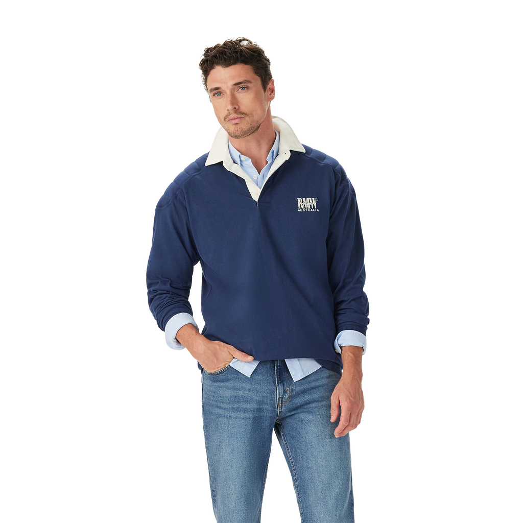 A man stands casually with one hand in his pocket, wearing the R.M.Williams Mens Mulyungarie 1/4 Zip Sweatshirt (KZU00BB03) in Vintage Blue over a light blue shirt and blue jeans, against a plain white background.