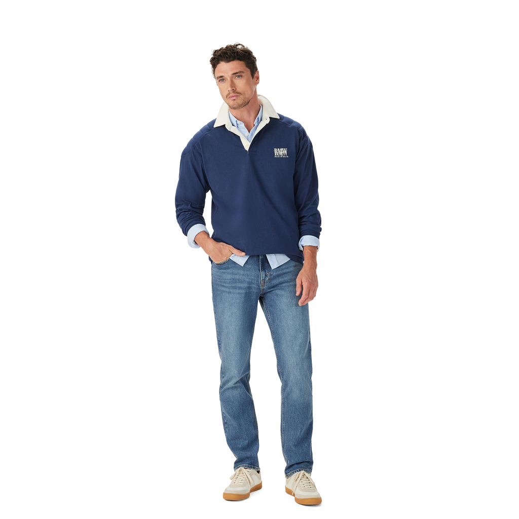 A man stands casually with one hand in his pocket, wearing the R.M.Williams Mens Mulyungarie 1/4 Zip Sweatshirt (KZU00BB03) in Vintage Blue over a light blue shirt and blue jeans, against a plain white background.