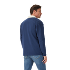 A man stands casually with his back partially to the camera, wearing the R.M.Williams Mens Mulyungarie 1/4 Zip Sweatshirt (KZU00BB03) in Vintage Blue over a light blue shirt and blue jeans, against a plain white background.