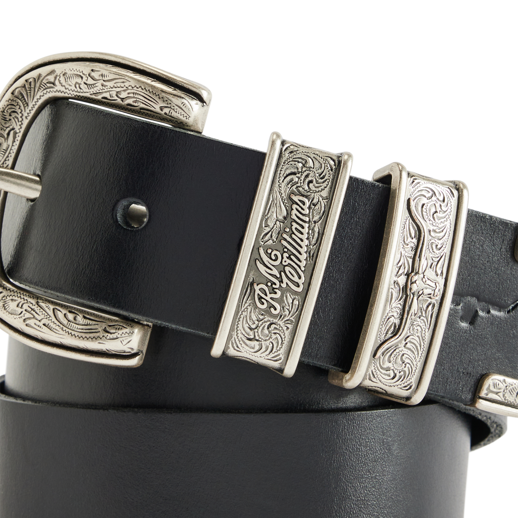 A coiled black R.M.Williams Western Drover Belt (BSF5DCH02) with engraved and embossed silver toned buckle and keepers on a white background.