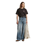 A woman wearing a dark chocolate R.M.Williams Kandos Short Sleeve Tee (KDX10JE06) with an RMW logo on the left chest, paired with denim jeans and a plaited leather belt, photographed on a white background.