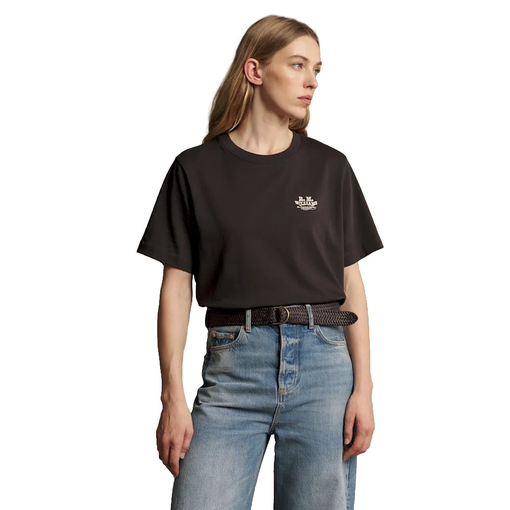 A woman wearing a dark chocolate R.M.Williams Kandos Short Sleeve Tee (KDX10JE06) with an RMW logo on the left chest, paired with denim jeans and a plaited leather belt, photographed on a white background.