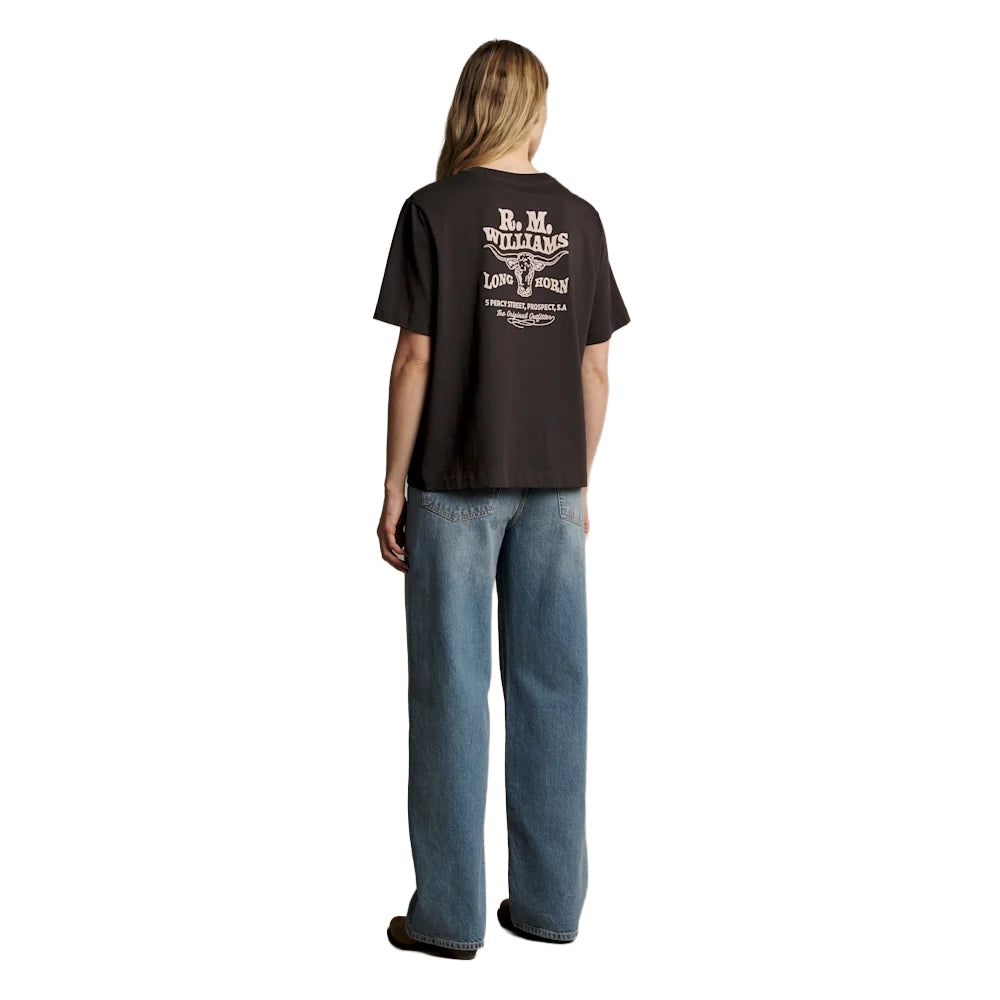 A woman from behind wearing a dark chocolate R.M.Williams Kandos Short Sleeve Tee (KDX10JE06) with a large back logo print of the RMW longhorn, paired with denim jeans, photographed on a white background.