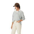 A woman in the R.M.Williams Womens Narran Heritage Rugby (Salt), featuring a light gray collared organic cotton design with Heritage logo embroidery, brown cap, and off-white pants stands with one hand in her pocket against a plain white background.