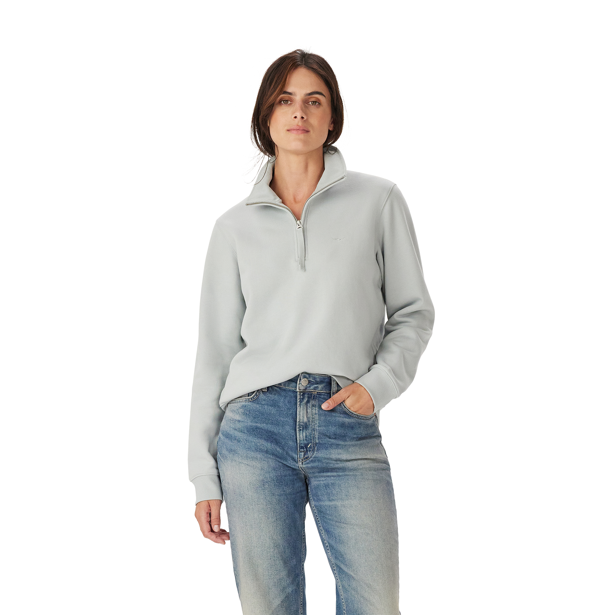 A woman with straight brown hair and a neutral expression wears the R.M.Williams Womens Trickett 1/4 Zip Sweatshirt (Salt) and blue jeans, standing against a plain white background with one hand in her pocket.
