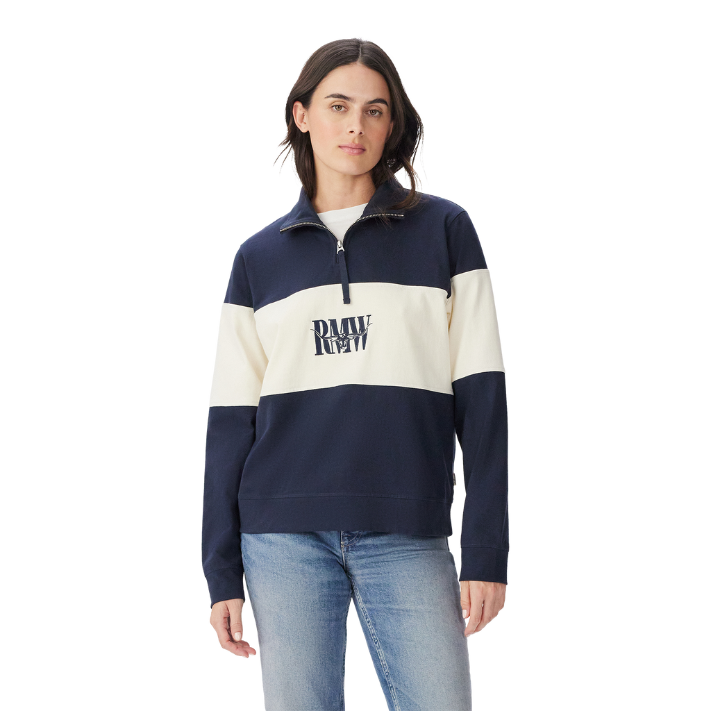 A person wears the R.M.Williams Womens Trickett Panel Sweatshirt (KZR00BB01) in French Navy, featuring navy and white colorblocking with "DRAW REV" text, paired with light blue jeans against a plain white background.