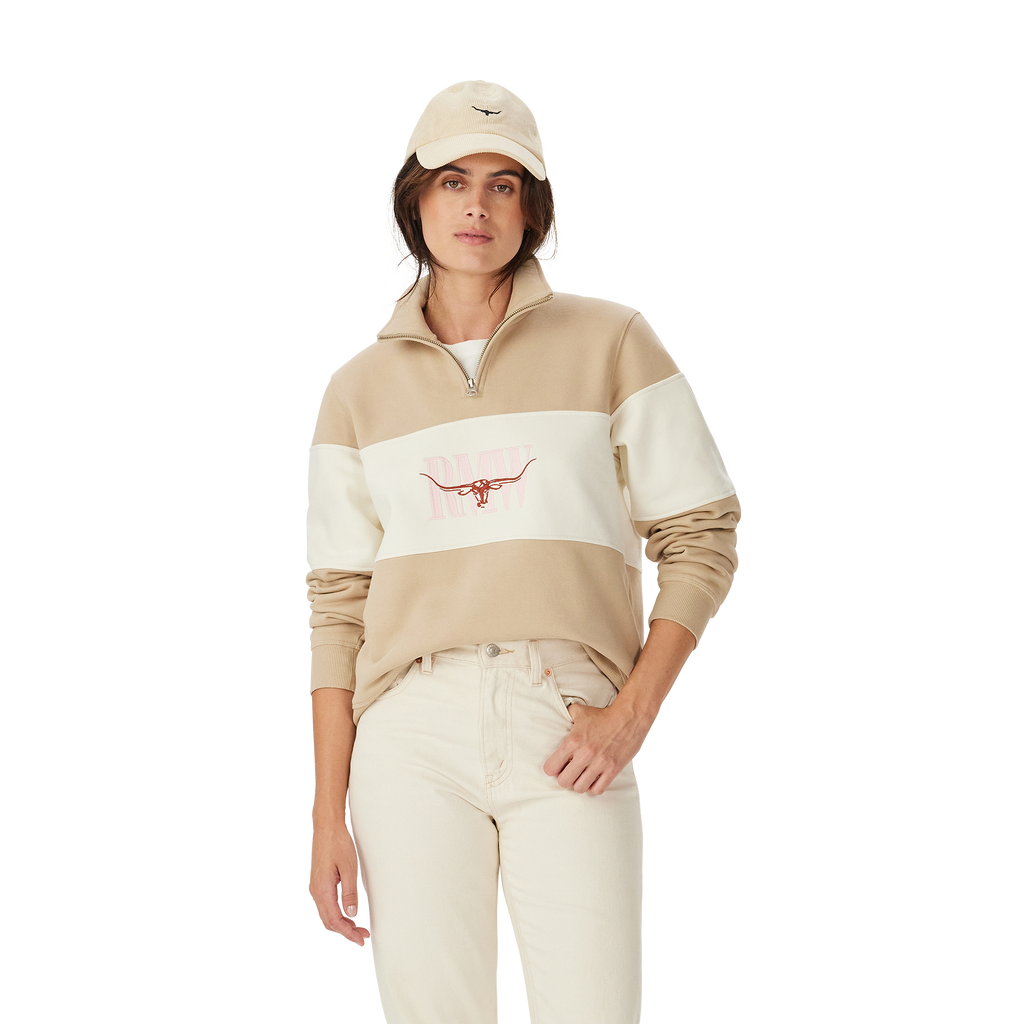 A woman in a beige cap, light jeans, and an R.M.Williams Womens Trickett Panel Sweatshirt (KZR00BB01) Sand stands against a plain white background.