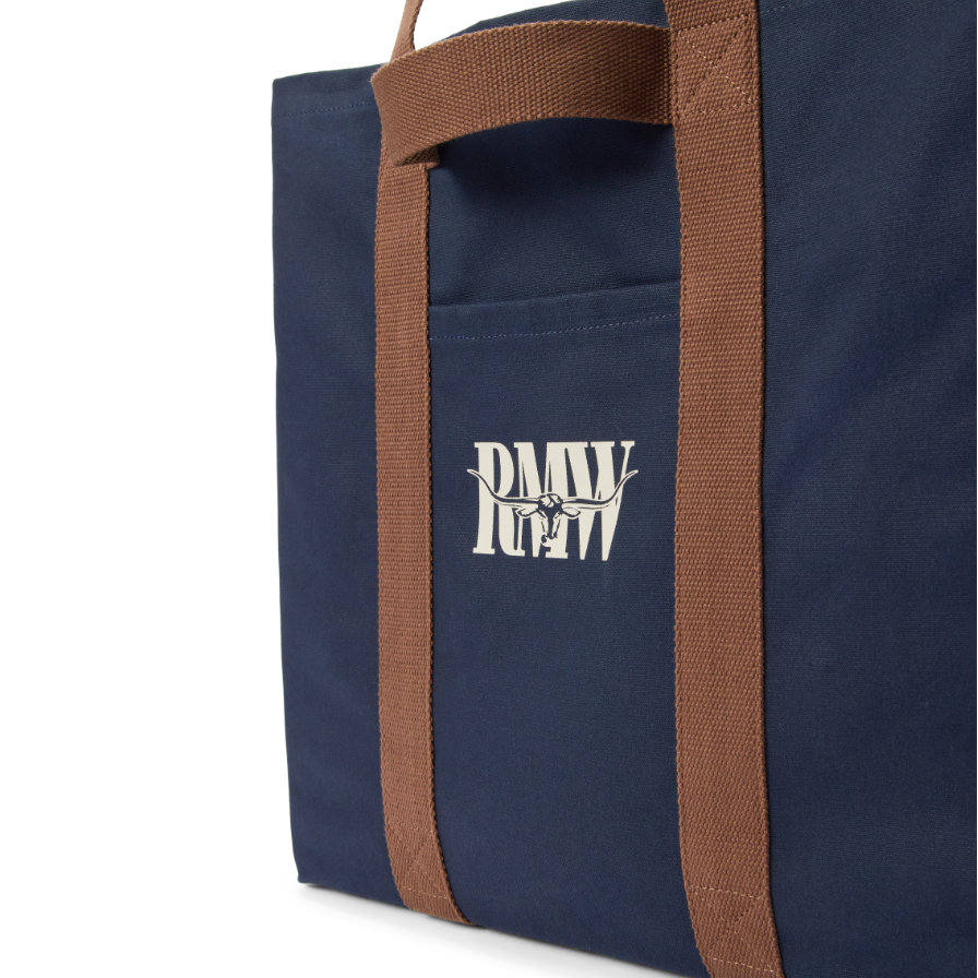 Close up detail of a navy R.M.Williams Heritage Tote (CGM9OCA04) with brown handles and RMW logo on a white background.