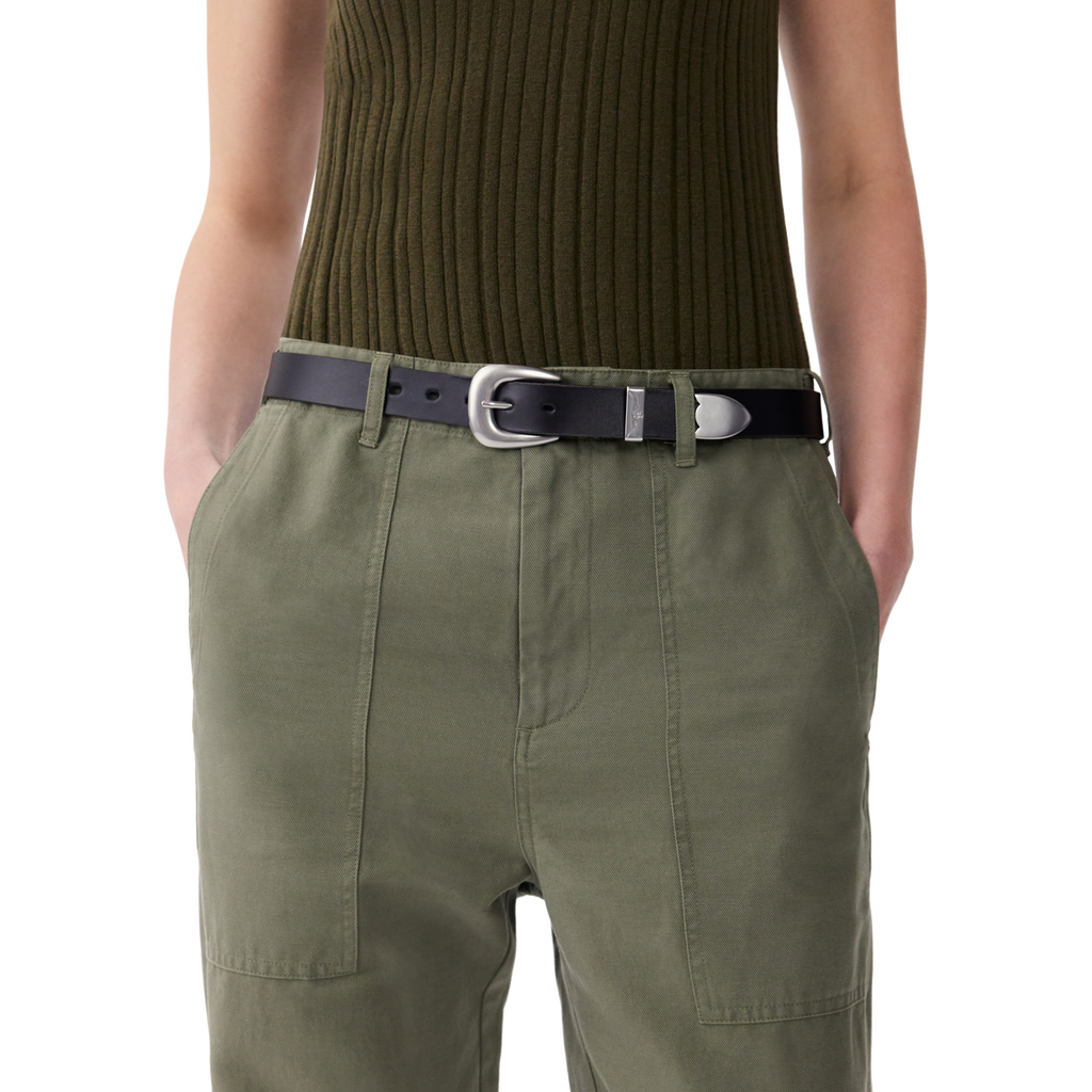 A woman wearing olive green pants with a black R.M.Williams Women's Cate Stitched Belt (BSC5FLE01) with a silver buckle on a white background.