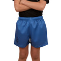 A child in a black shirt and Ringers Western Childrens Big Ringers Footy Shorts (325020RW) Blue stands arms crossed. The blue shorts, branded by Ringers Western, have an elastic waistband, left-leg emblem, and durable design. Face not visible.