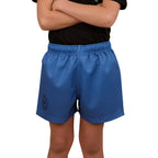 A child in a black shirt and Ringers Western Childrens Big Ringers Footy Shorts (325020RW) Blue stands arms crossed. The blue shorts, branded by Ringers Western, have an elastic waistband, left-leg emblem, and durable design. Face not visible.