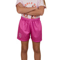 A child with arms crossed wears a light pink T-shirt and Ringers Western Childrens Big Ringers Footy Shorts (Candy), featuring the brand's emblem on the left leg. The child's face is not visible.