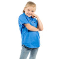 A young girl with blonde hair in a ponytail smiles at the camera against a white background, wearing the Ringers Western Childrens Ord Half Button S/S Work Shirt (321010RW) in blue with light jeans.