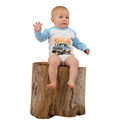 A baby wearing the Ringers Western Infants Trucker Kid L/S Romper in White/Blue sits on a large tree stump with one hand raised, gazing to the side against a plain white background.