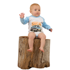A baby wearing the Ringers Western Infants Trucker Kid L/S Romper in White/Blue sits on a large tree stump with one hand raised, gazing to the side against a plain white background.