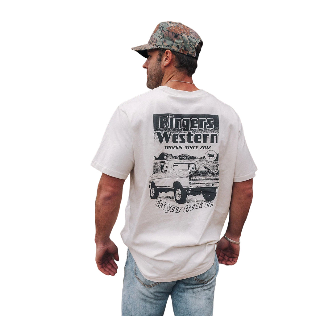 A man wears the Ringers Western Mens Get Your Truck On Loose Fit S/S Tee in off white, featuring a truck graphic and logo on the back, paired with a camo cap and light blue jeans—ideal country style from Ringers Western.