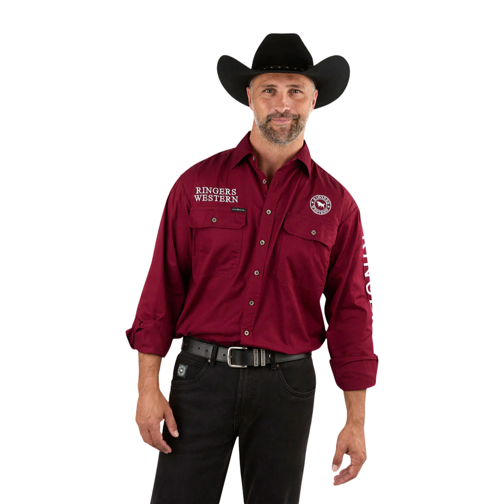 A man wearing a black cowboy hat and the Ringers Western Mens Hawkeye Full Button L/S Work Shirt (118110002) in Burgundy, featuring "Ringers Western" logos, stands smiling with one hand by his side, paired with black pants.