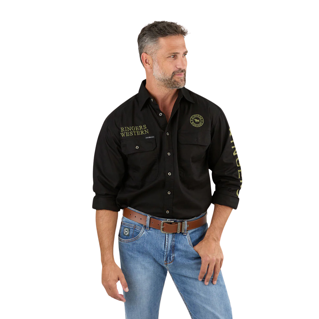 A man wears the Ringers Western Mens Hawkeye Full Button L/S Work Shirt (118110002) in Black/Camo with light blue jeans and a brown belt. He has short hair, a trimmed beard, rolled-up sleeves, and looks off to the side.
