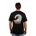 A man wears a black Ringers Western Mens Reef and Beef Loose Fit S/S Tee with a large surfer graphic and "RANCH WATER" text on the back, standing away to showcase the bold cotton crew neck design.
