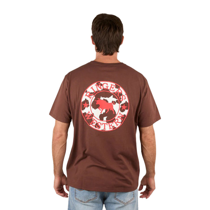 A man stands with his back to the camera in light blue jeans, wearing a loose fit Ringers Western Mens Signature Bull S/S Tee (Chocolate/Red/Cow Print) featuring a large red and white logo and cow graphic on the back.