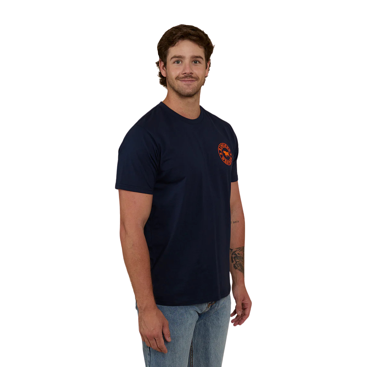 A man wearing a navy blue Ringers Western Men's Signature Bull Loose Fit S/S Tee (120201560) with an orange circular graphic that reads 'Ringers Western' with a bull silhouette, paired with blue jeans against a plain white background.