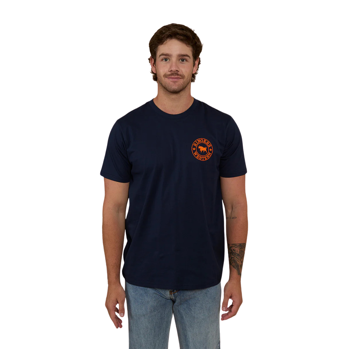 A man wearing a navy blue Ringers Western Men's Signature Bull Loose Fit S/S Tee (120201560) with an orange circular graphic that reads 'Ringers Western' with a bull silhouette, paired with blue jeans against a plain white background.