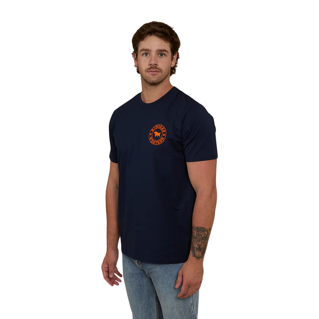 A man wearing a navy blue Ringers Western Men's Signature Bull Loose Fit S/S Tee (120201560) with an orange circular graphic that reads 'Ringers Western' with a bull silhouette, paired with blue jeans against a plain white background.