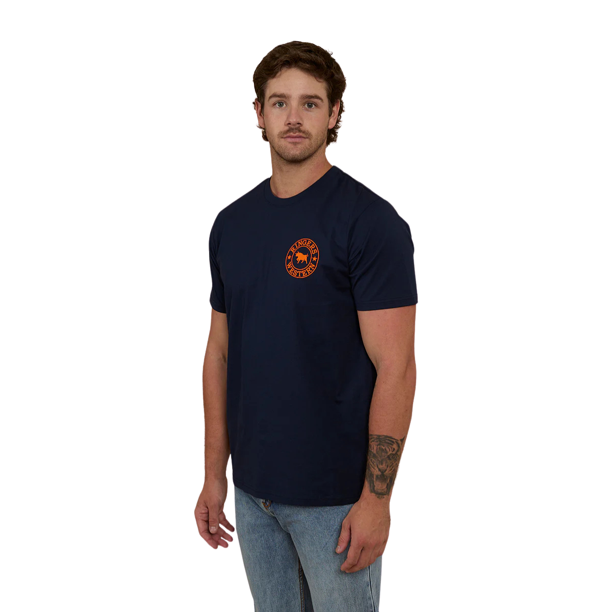 A man wearing a navy blue Ringers Western Men's Signature Bull Loose Fit S/S Tee (120201560) with an orange circular graphic that reads 'Ringers Western' with a bull silhouette, paired with blue jeans against a plain white background.